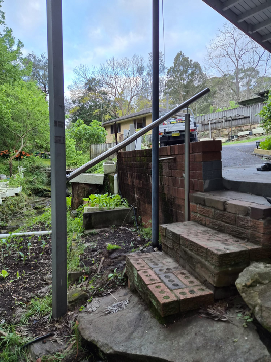 Freestanding stainless steel handrail installed beside outdoor brick steps